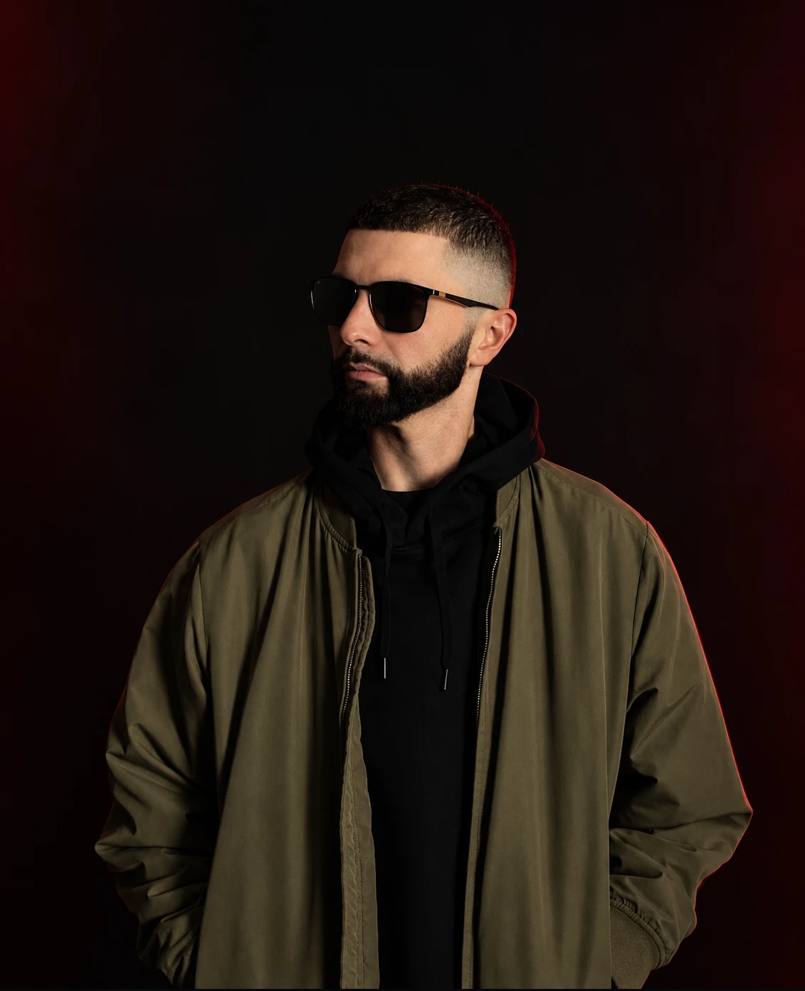 RESON in sunglasses and an olive jacket with subtle red studio lighting